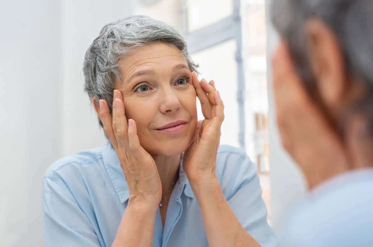 Aging woman checking for dark circles in mirror